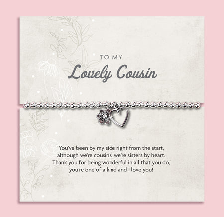 A silver beaded bracelet with a heart and flower charm displayed on a card reading 