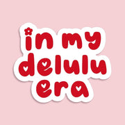 Red text 'in my delulu era' on a pink background. Cute aesthetic sticker for journals or water bottles.