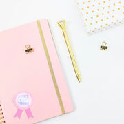 Pink notebook with gold accents and a gold pen on a white background with a 'didnt cry today sticker'