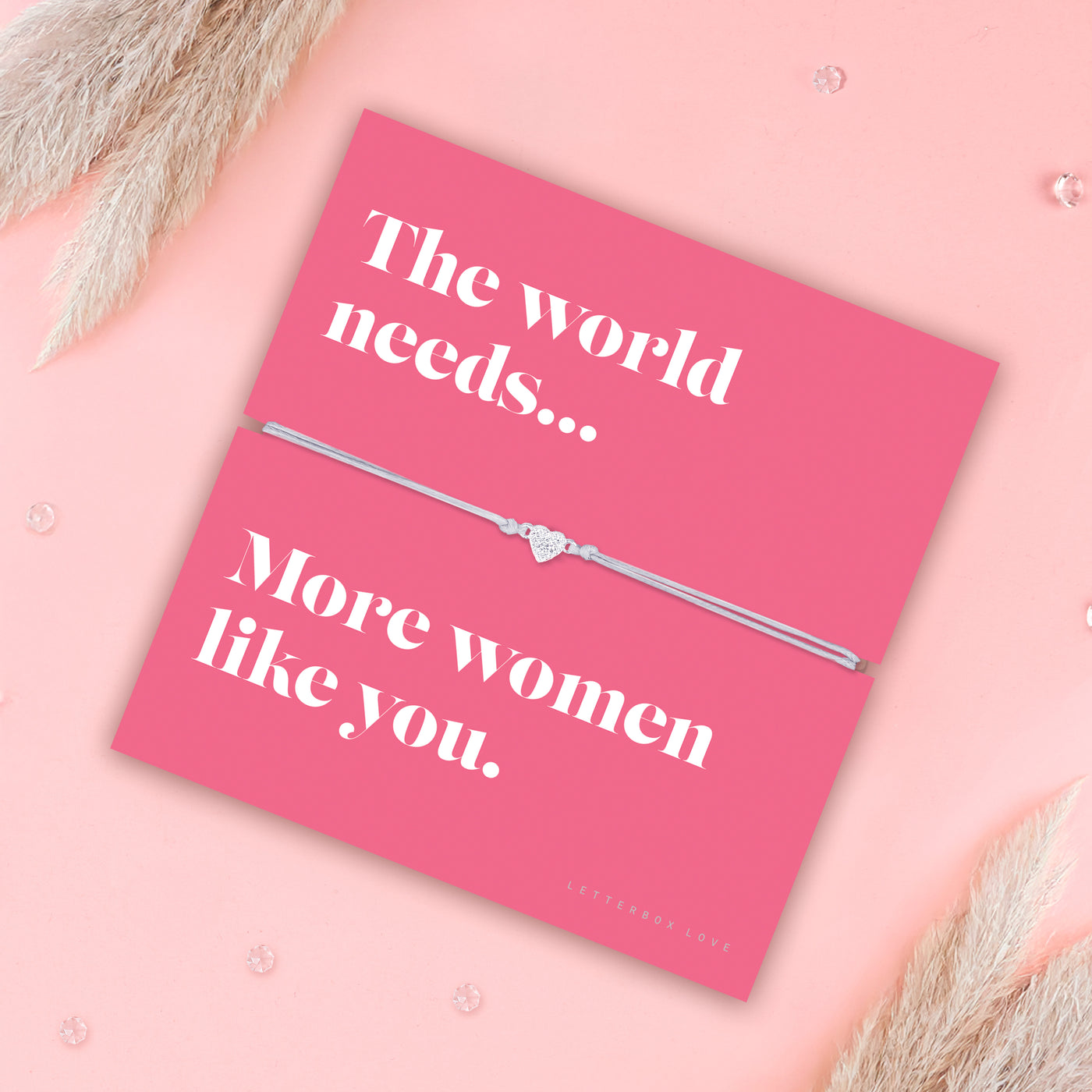 Friendship bracelet with a silver heart charm on an adjustable cord, displayed on a pink card reading “The world needs… more women like you” — an empowering bracelet for a friend and thoughtful friendship gift by Letterbox Love. With pampus grass.