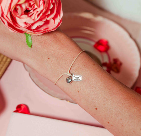 Bracelet with heart and letter charm on wrist, pink flower in background