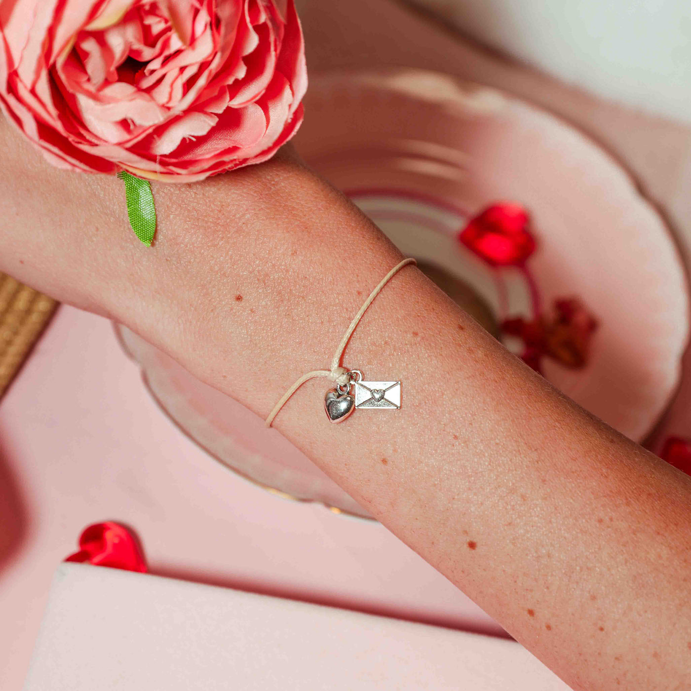Bracelet with heart and letter charm on wrist, pink flower in background