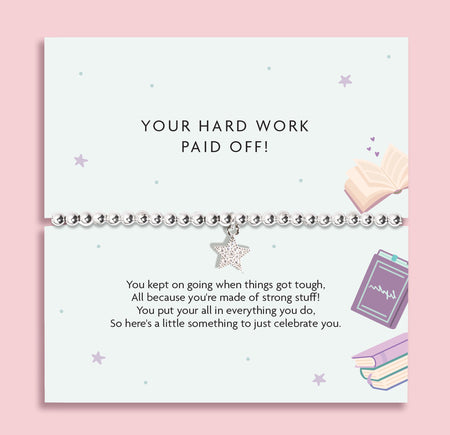 A silver beaded bracelet with a dangling rhinestone star charm, presented on a white card that reads 'YOUR HARD WORK PAID OFF!' with motivational text, set against a soft pink background.