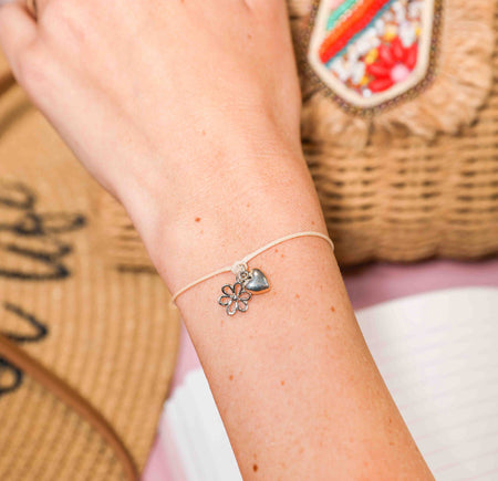 Close-up of a wrist wearing a bracelet with flower and heart charms against a blurred background