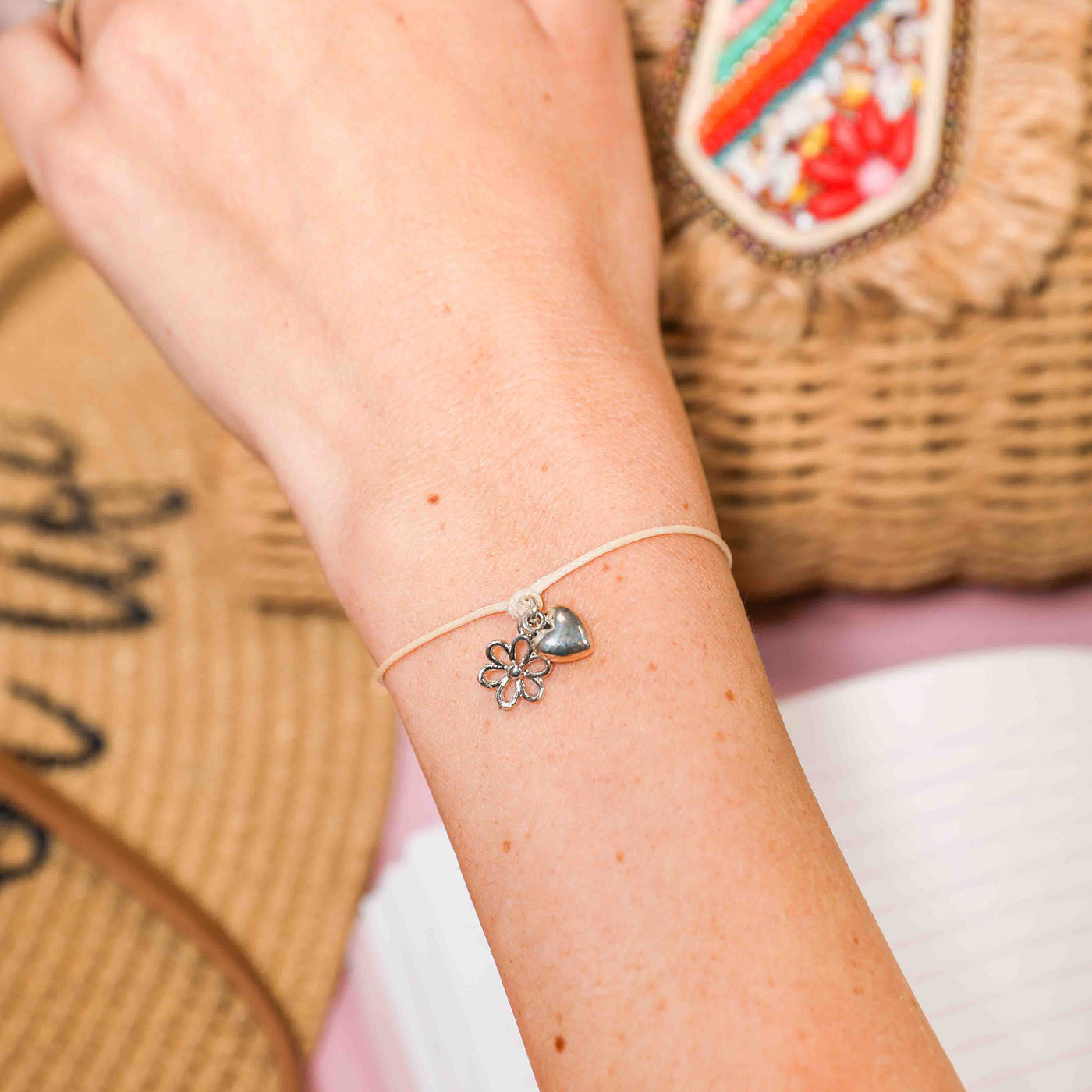 Close-up of a wrist wearing a bracelet with flower and heart charms against a blurred background
