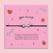 Adjustable black cord Gym Bunny bracelet with silver dumbbell charm displayed on pink motivational fitness message card, workout and gym gift for her.