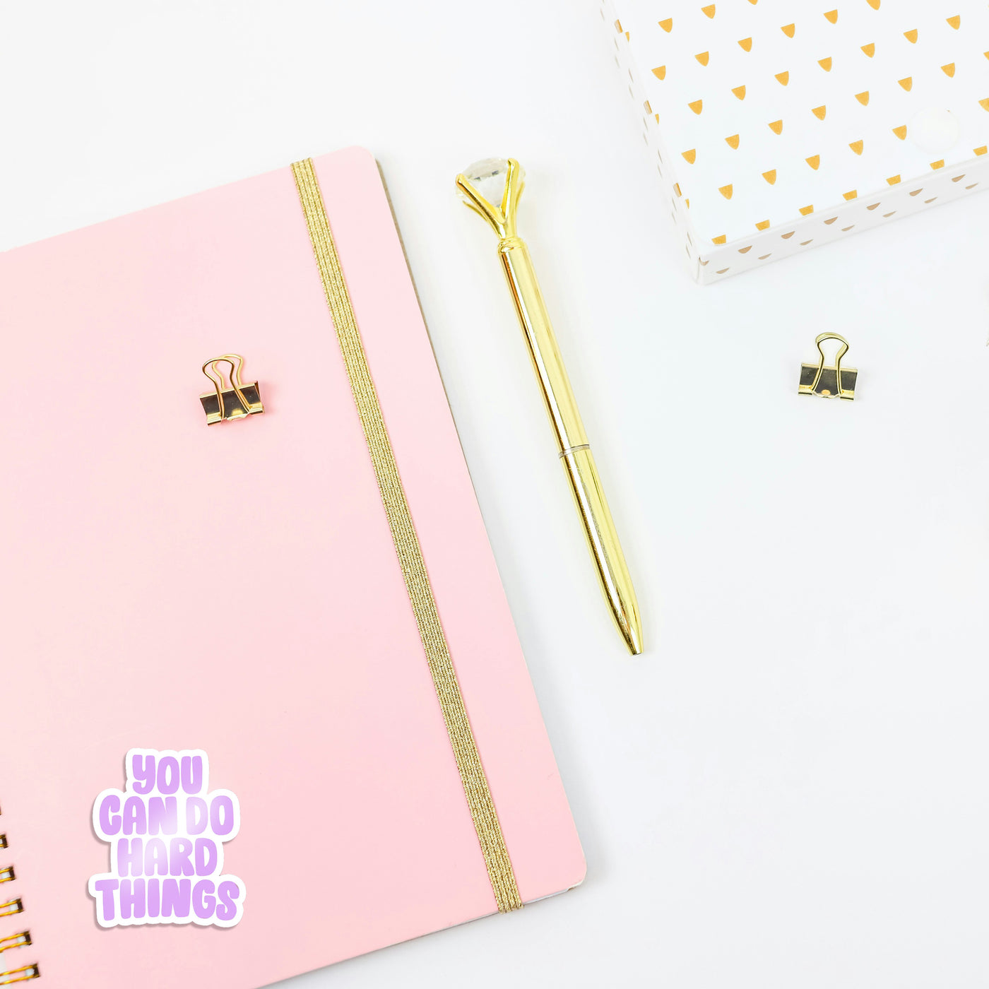 Pink notebook with gold accents and a gold pen on a white background, with a 'you can do hard things' sticker