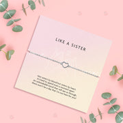 a pink background with a like a sister poem card and silver-plated hollow heart bracelet surrounded by eucalyptus