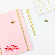 Pink notebook with gold accents and a gold pen on a white background