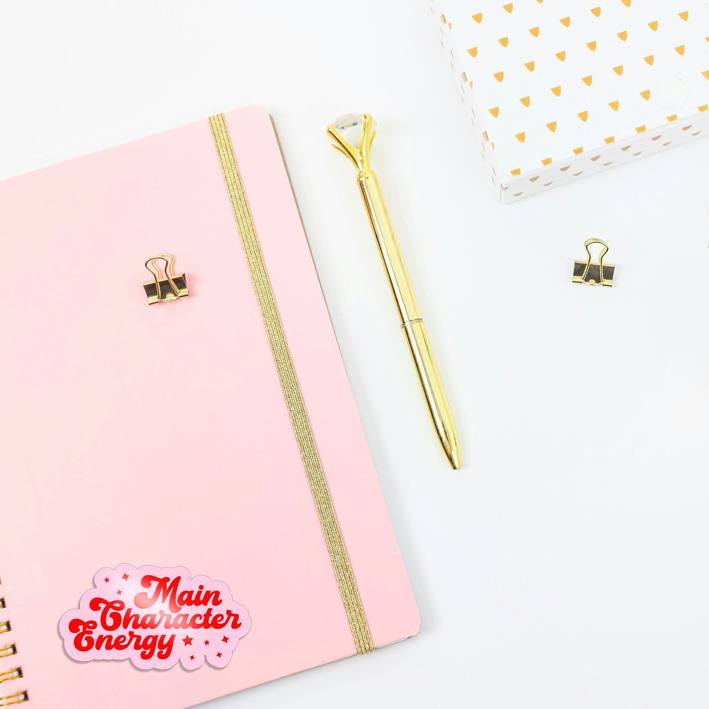 Pink notebook with gold accents and a gold pen on a white background