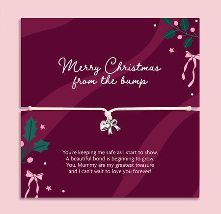 A Christmas gift with a bracelet across the center holding a small silver bow charm. The card is deep burgundy with white script text reading 'Merry Christmas from the bump' and additional holiday illustrations, shown against a light pink background.