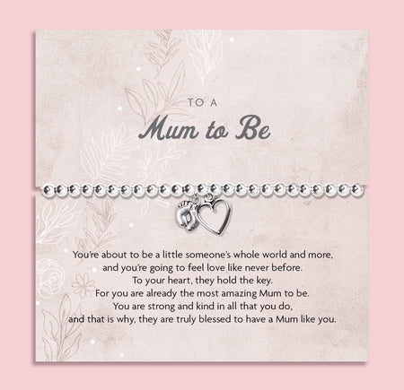 A silver beaded bracelet with a small heart and footprint charm, presented on a personalized 'Mum to Be' card with a quote, set against a solid pink background.