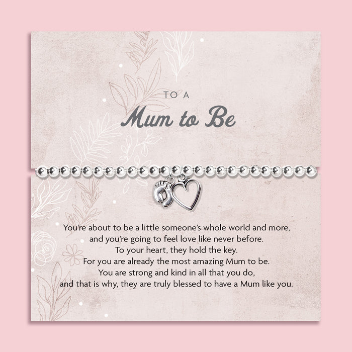 A silver beaded bracelet with a small heart and footprint charm, presented on a personalized 'Mum to Be' card with a quote, set against a solid pink background.
