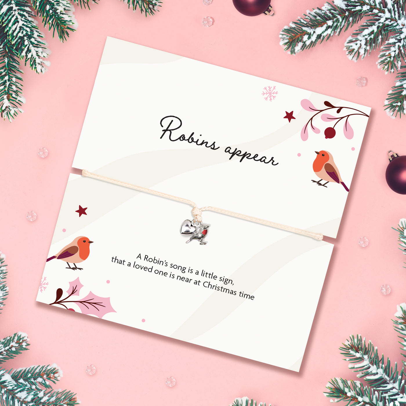 A Christmas-themed card with a thin adjustable bracelet, featuring robin illustrations and the text 'Robins appear' and a poem. The card is styled on a pink background with pine branches and ornaments.
