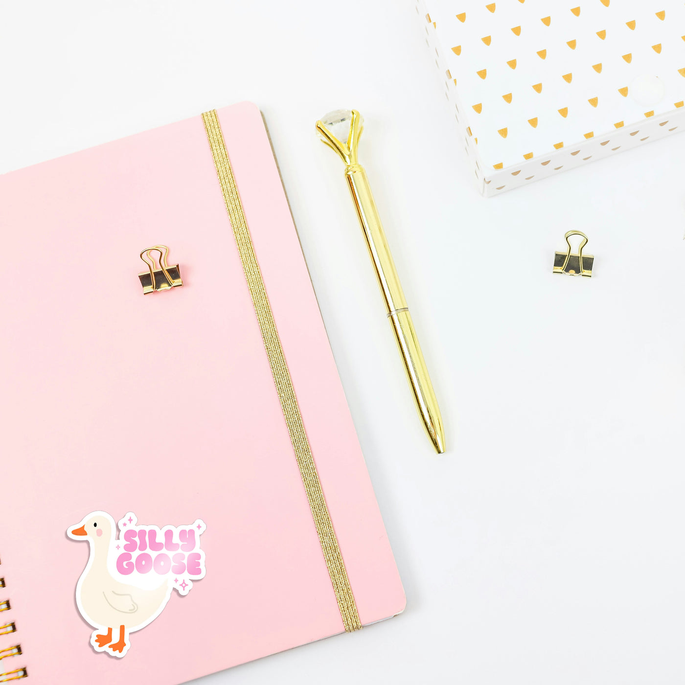 Pink notebook with gold accents and a gold pen on a white background, featuring 'Silly Goose' sticker.