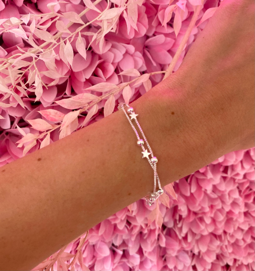 a pink floral background with a woman's wrist wearing the layered silver stars bracelet