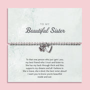 Silver beaded bracelet with heart and flower charms, displayed in a white gift box alongside a card titled "To My Beautiful Sister." The card features a heartfelt message celebrating the love and support of a cherished sister.