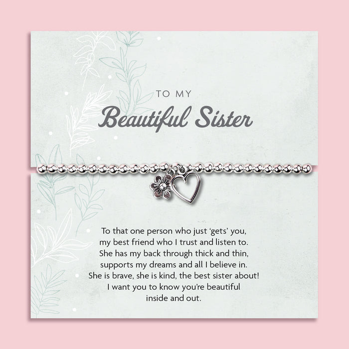 Silver beaded bracelet with heart and flower charms, displayed in a white gift box alongside a card titled "To My Beautiful Sister." The card features a heartfelt message celebrating the love and support of a cherished sister.