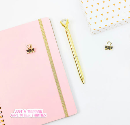 Pink notebook with gold accents and a gold pen on a white background
