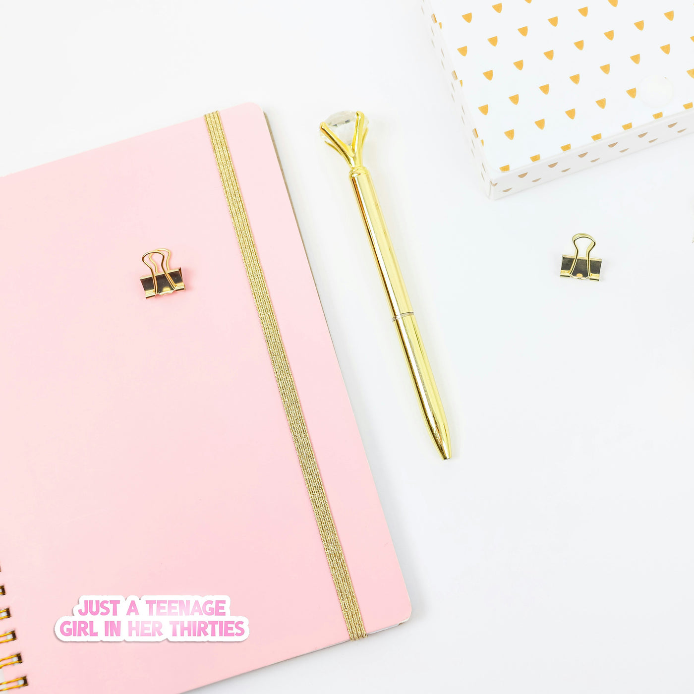 Pink notebook with gold accents and a gold pen on a white background