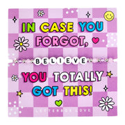 An image of a motivational card featuring a beaded bracelet with white letter beads spelling "BELIEVE." The card has a purple checkered background with bold, colorful text that reads: "In case you forgot, you totally got this!" The design includes playful illustrations of smiley faces, hearts, flowers, and stars, creating a vibrant and encouraging theme. A fun and uplifting gift designed to boost the recipient's confidence and remind them of their strength and ability to succeed.
