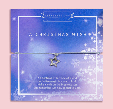 A Christmas Wish bracelet packaging with a pale grey-colored adjustable string bracelet displayed in the background, surrounded by Christmas decorations like balls and trees.