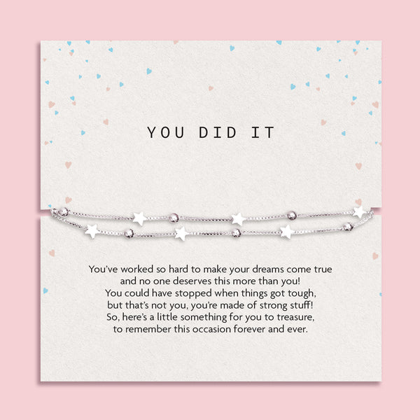Motivational card titled "YOU DID IT" featuring a delicate silver-plated double chain bracelet with star and bead charms. The background is a soft cream tone with pastel heart confetti scattered around. A heartfelt message below the bracelet celebrates perseverance and achievement, making it a meaningful gift to mark a special milestone or success.