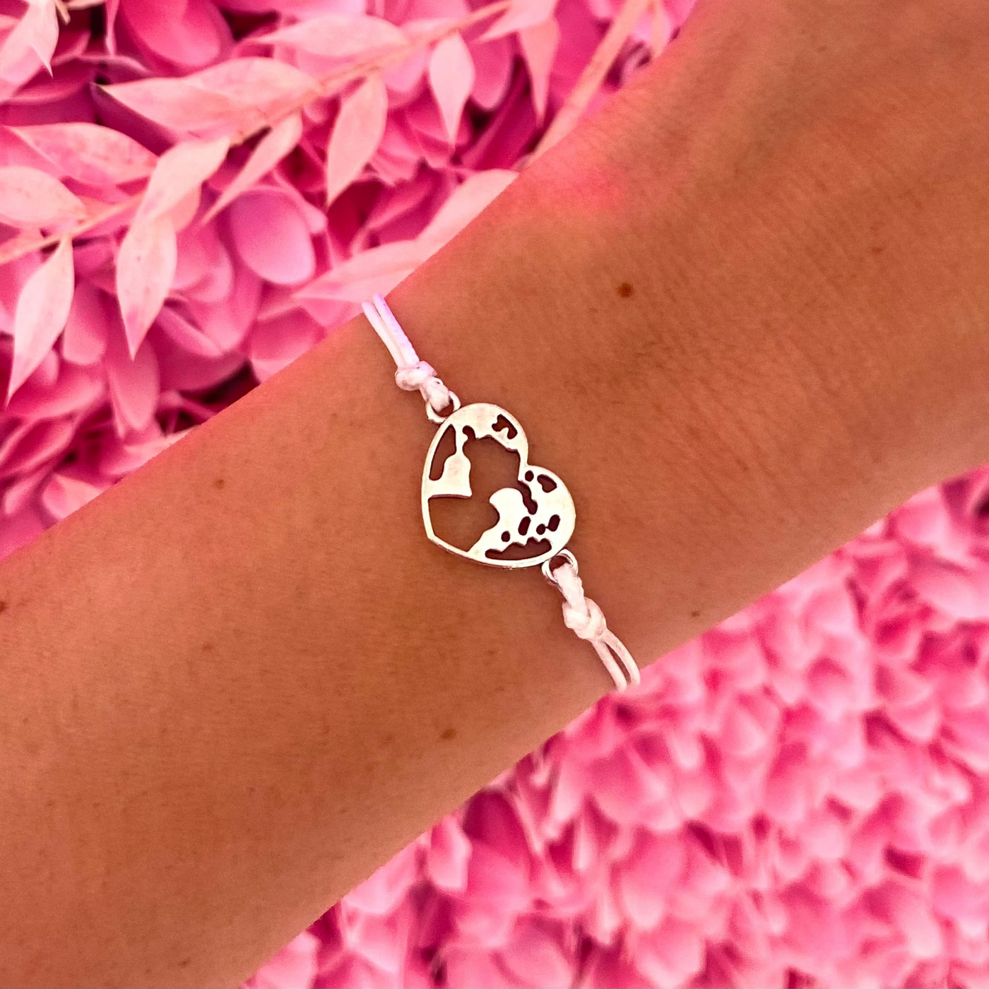 Bracelet with heart-shaped globe charm on wrist against pink floral background.