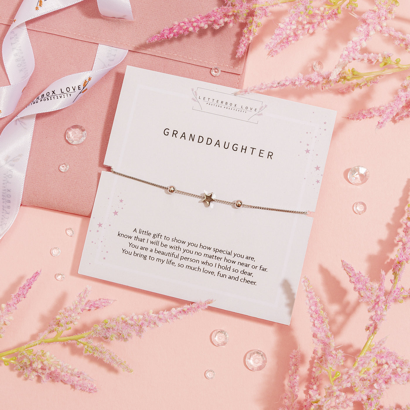 A delicate bracelet gift for a granddaughter, presented on a 'Letterbox Love' card with a touching poem. The bracelet features a central star charm flanked by two small beads on a silver chain, symbolizing love and guidance. The card and bracelet are designed with a subtle pink starry background, conveying affection and tenderness.