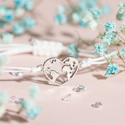 A pale pink background with small blue flowers and a white adjustable friendship bracelet with a silver-plated globe heart charm. Perfect for a travel gift.