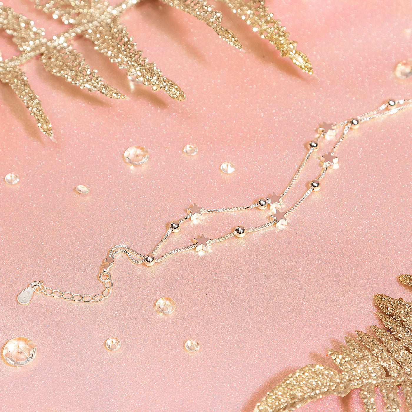 A sparkly pink background with gems and a silver star bracelet. A dainty bracelet gift for her. 