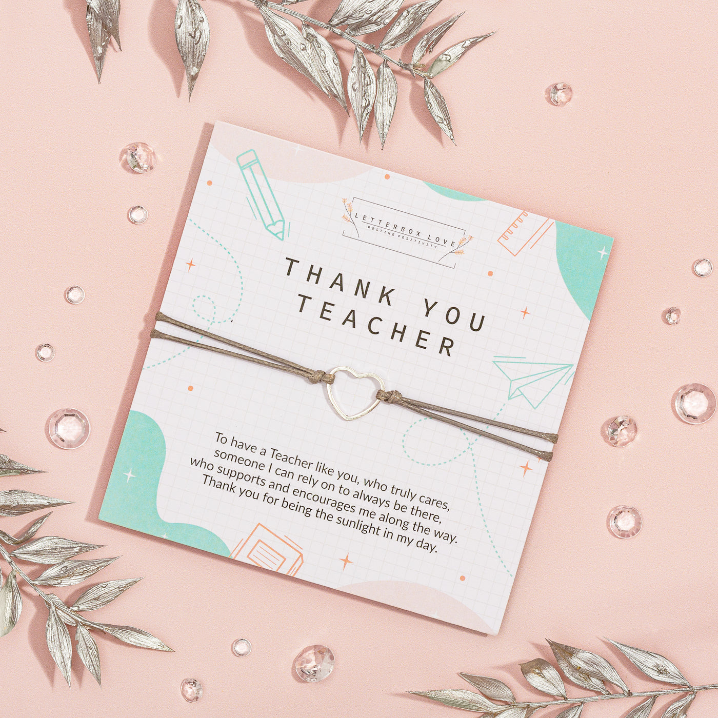 Appreciative 'Thank You Teacher' card on a soft pink background, adorned with geometric and school-related illustrations. The card features heartfelt gratitude text and is accompanied by a delicate bracelet with a heart charm.