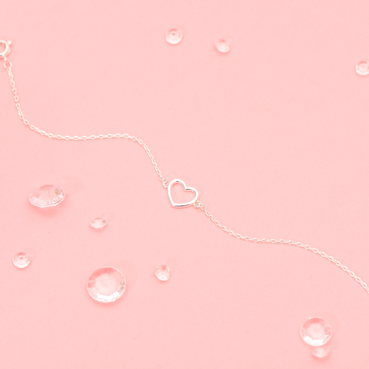 A pink background with an elegant silver-plated heart bracelet and crystal gems.