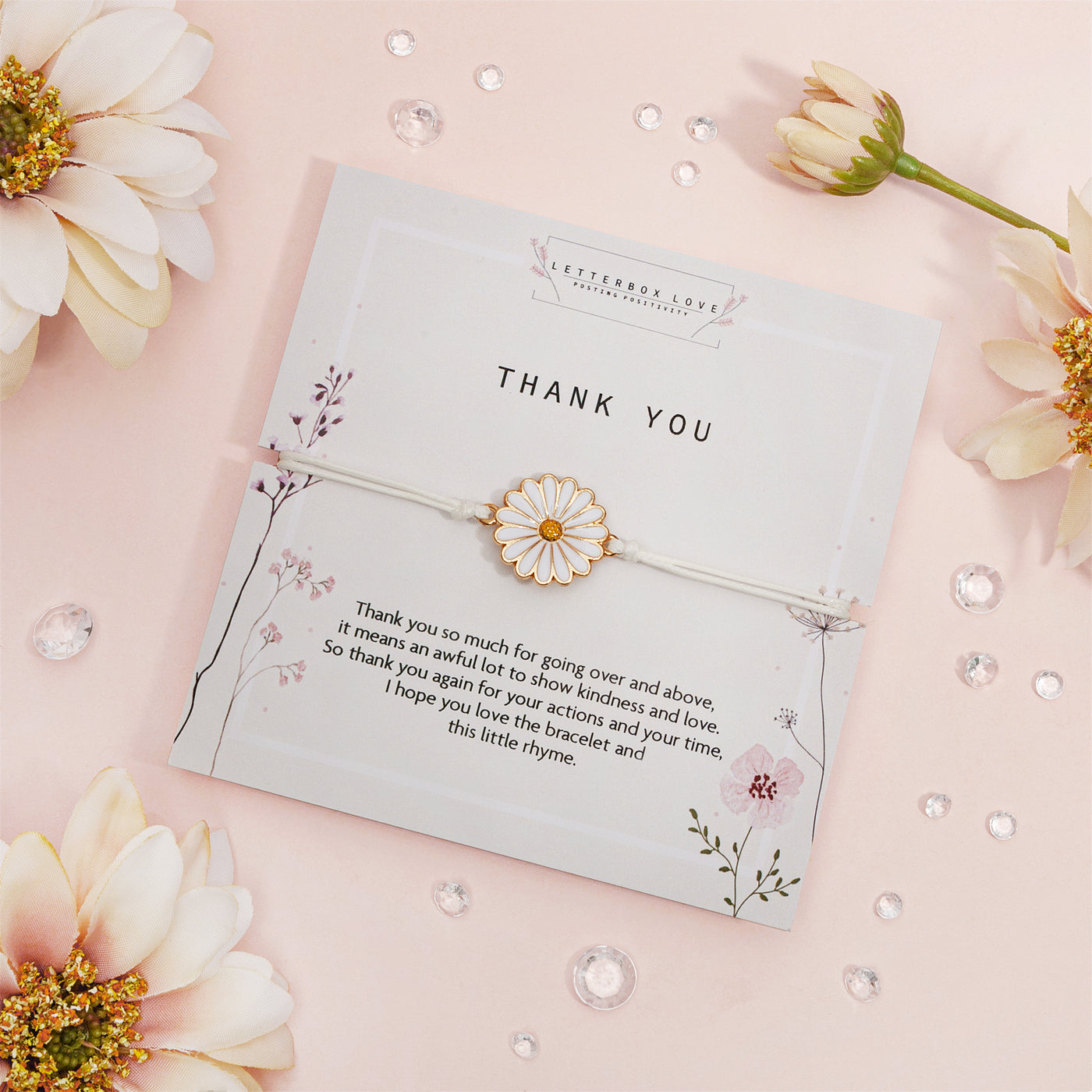 Elegant 'Thank You' card on a blush pink backdrop, adorned with a daisy-inspired bracelet. The card showcases delicate floral illustrations and a heartfelt gratitude message. 