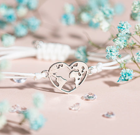 A pink background with a globe heart charm bracelet and blue flowers