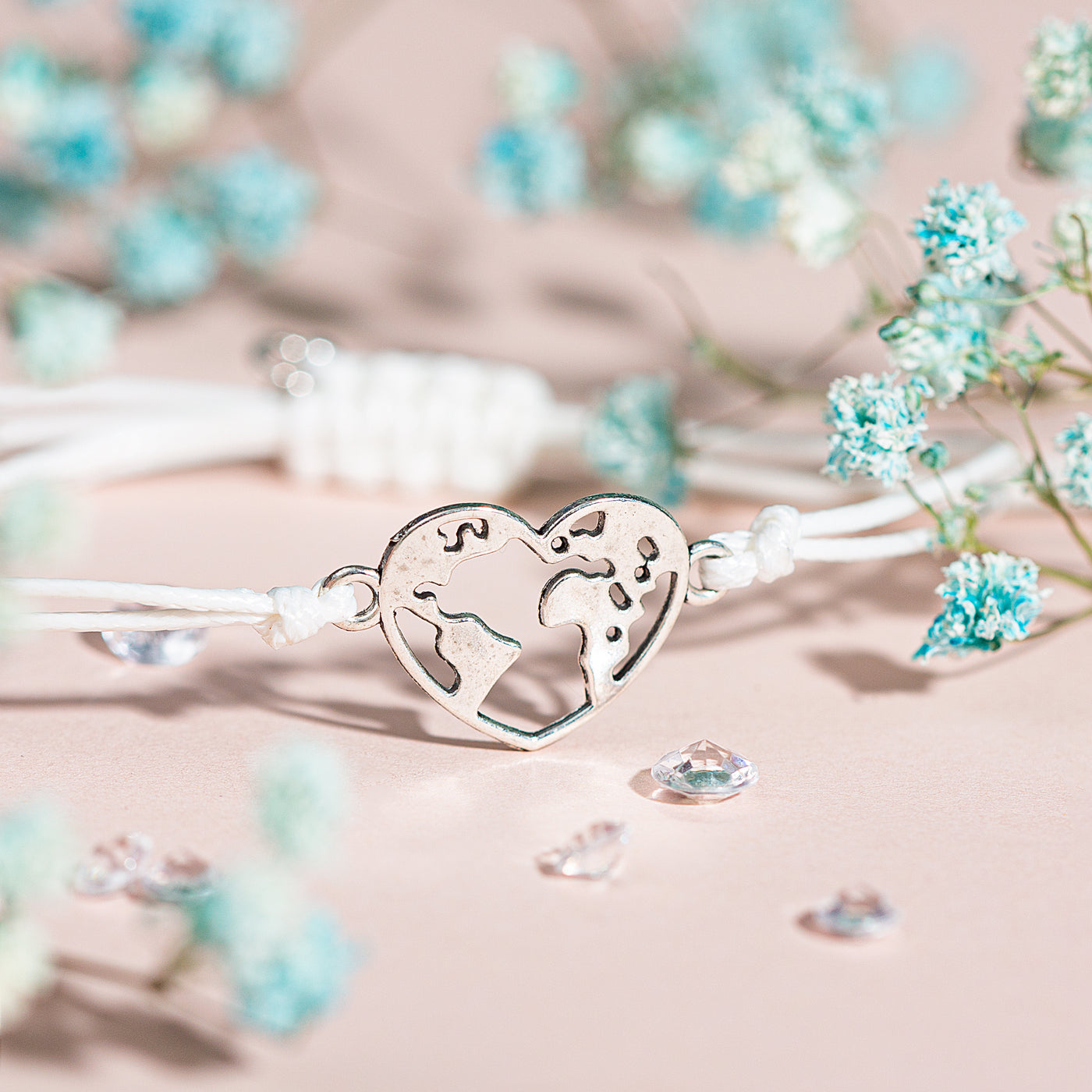 A pink background with a globe heart charm bracelet and blue flowers