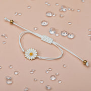 A pale peach background with scattered gems and a pretty daisy charm bracelet. The cord is adjustable with gold details. A pretty bracelet for a friend.
