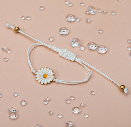 A pale peach background with scattered gems and a pretty daisy charm bracelet. The cord is adjustable with gold details. A pretty bracelet for a friend.