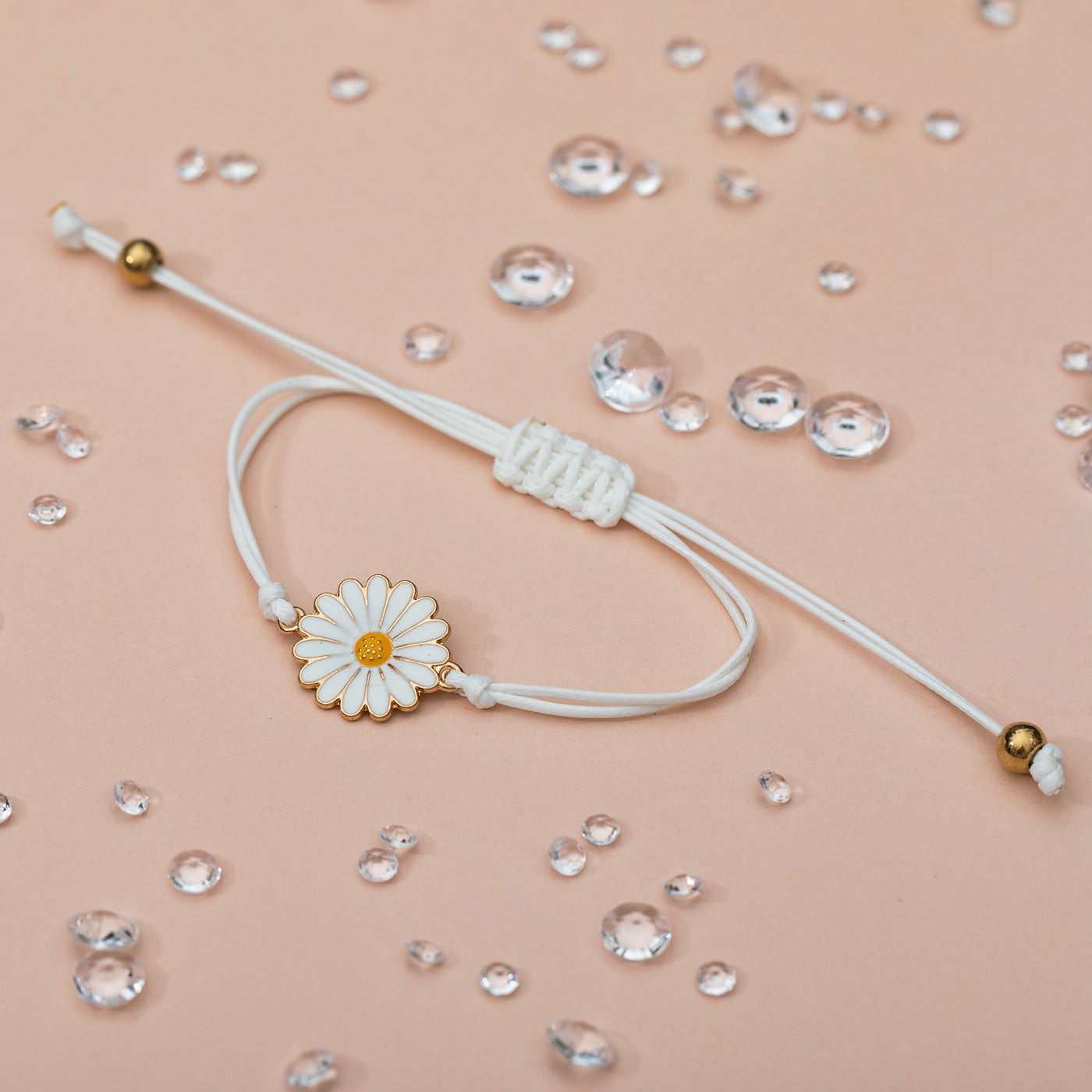 A pale peach background with scattered gems and a pretty daisy charm bracelet. The cord is adjustable with gold details. A pretty bracelet for a friend.