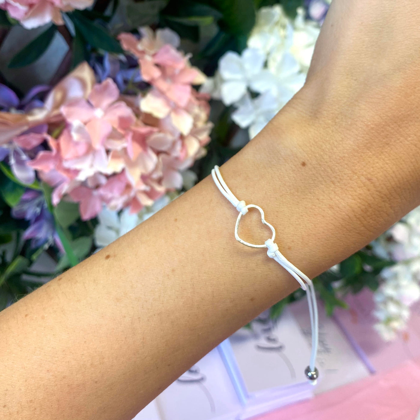 a woman's wrist with a white string bracelet and a floral background